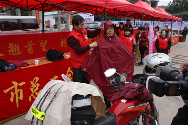 梧州市總工會的黨員義工們在市東出口春運(yùn)服務(wù)站助力“摩托大軍”平安返鄉(xiāng)，幫助他們檢查車輛和行李，穿上雨衣。--黃賀峰攝.j